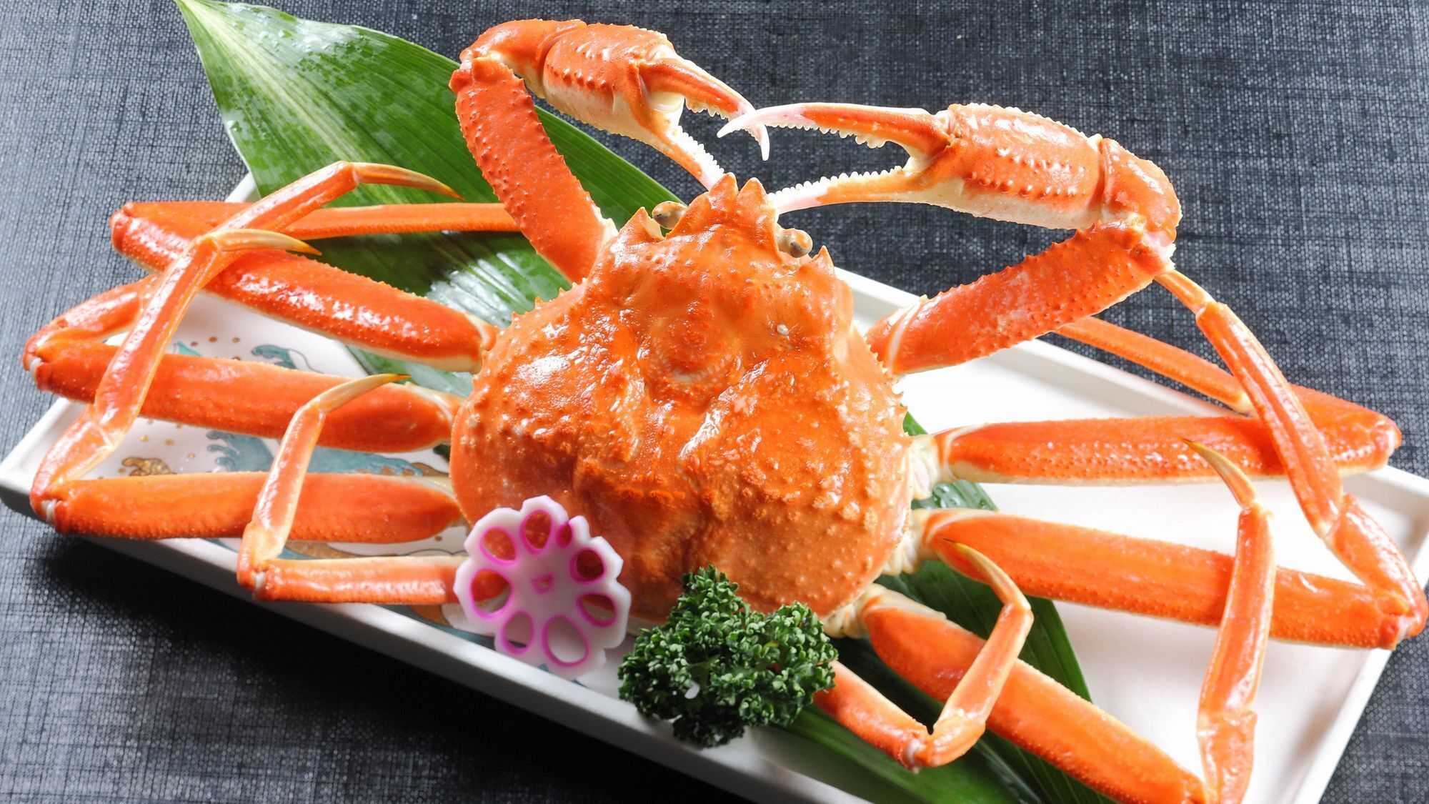 A crab dish on a white plate with green leaves and a purple garnish.