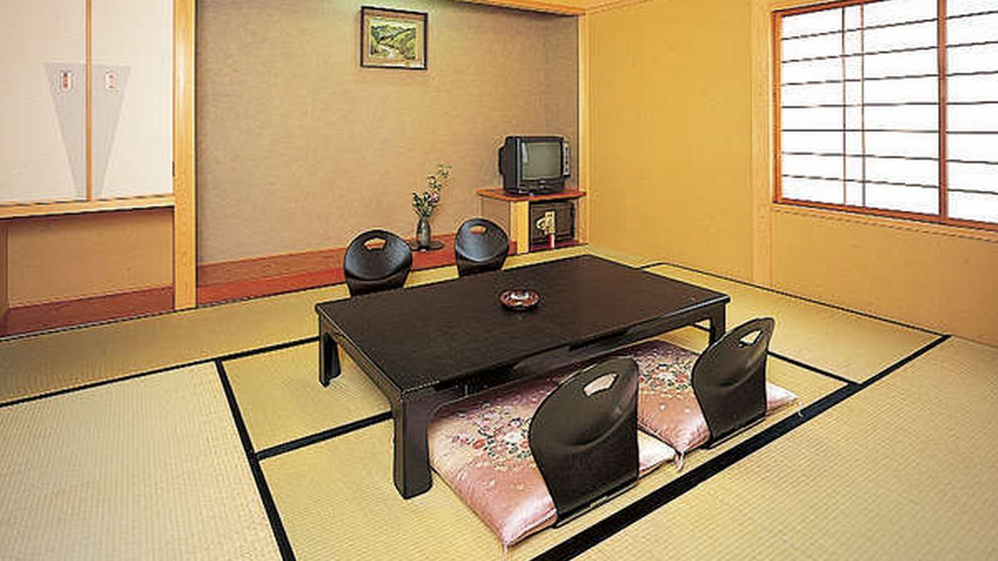 A tatami mat room with a low table, chairs, a television, and a small cabinet.