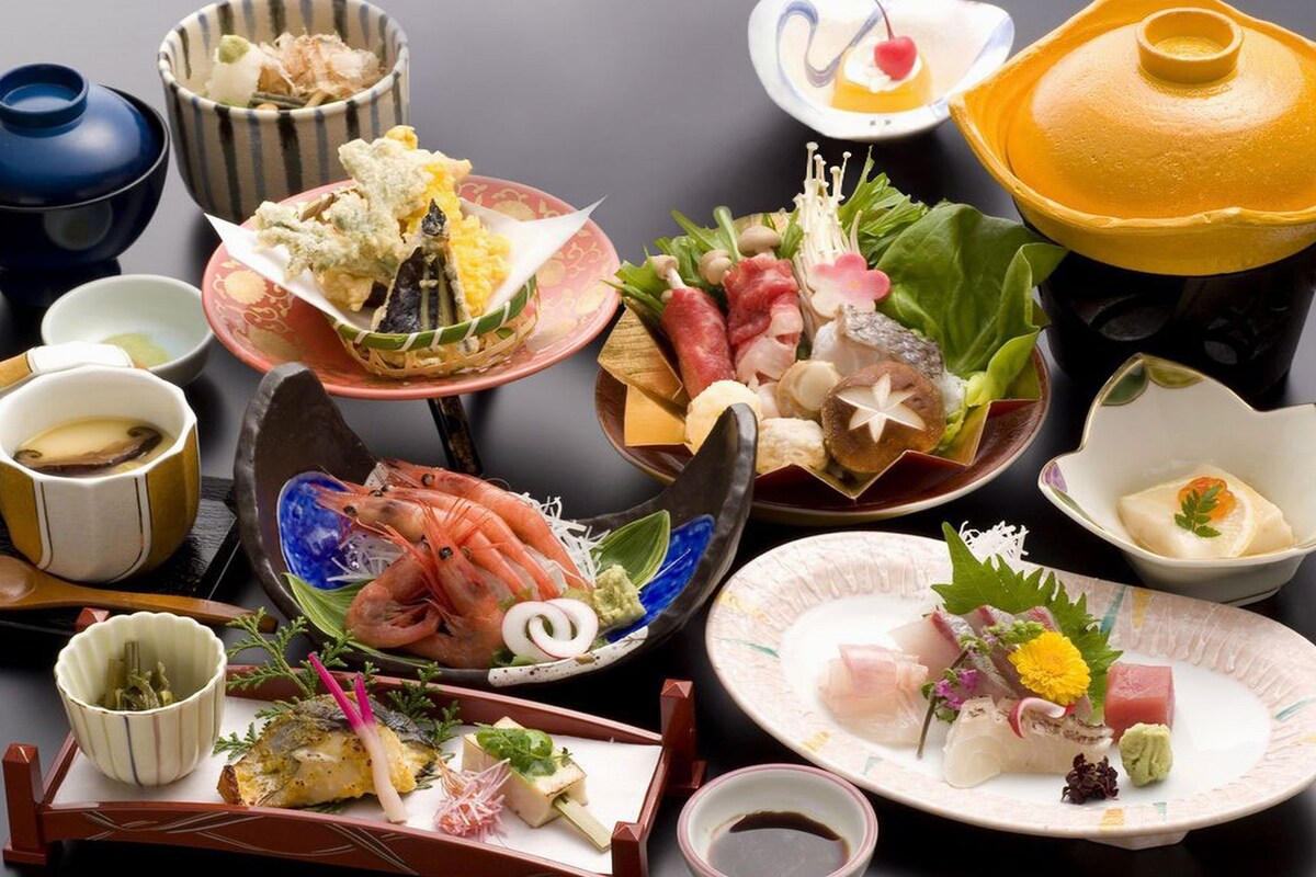 Eine Auswahl japanischer Gerichte auf einem Tisch, darunter Sushi, Sashimi und weitere Köstlichkeiten, mit kleinen Schälchen und einer Teekanne.