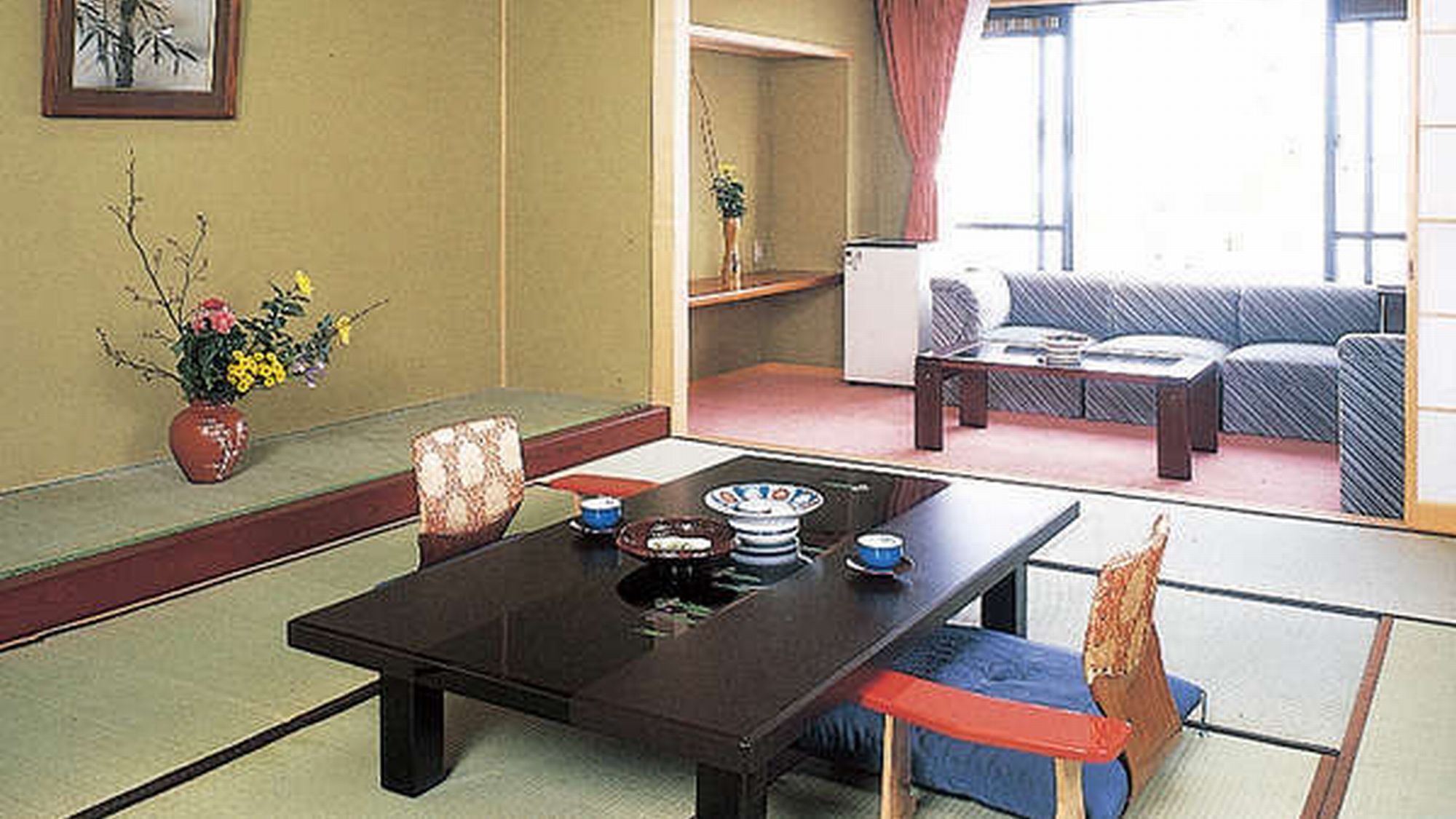 A traditional Japanese room with tatami flooring, a low table with dishes, a sofa, and a window with curtains.