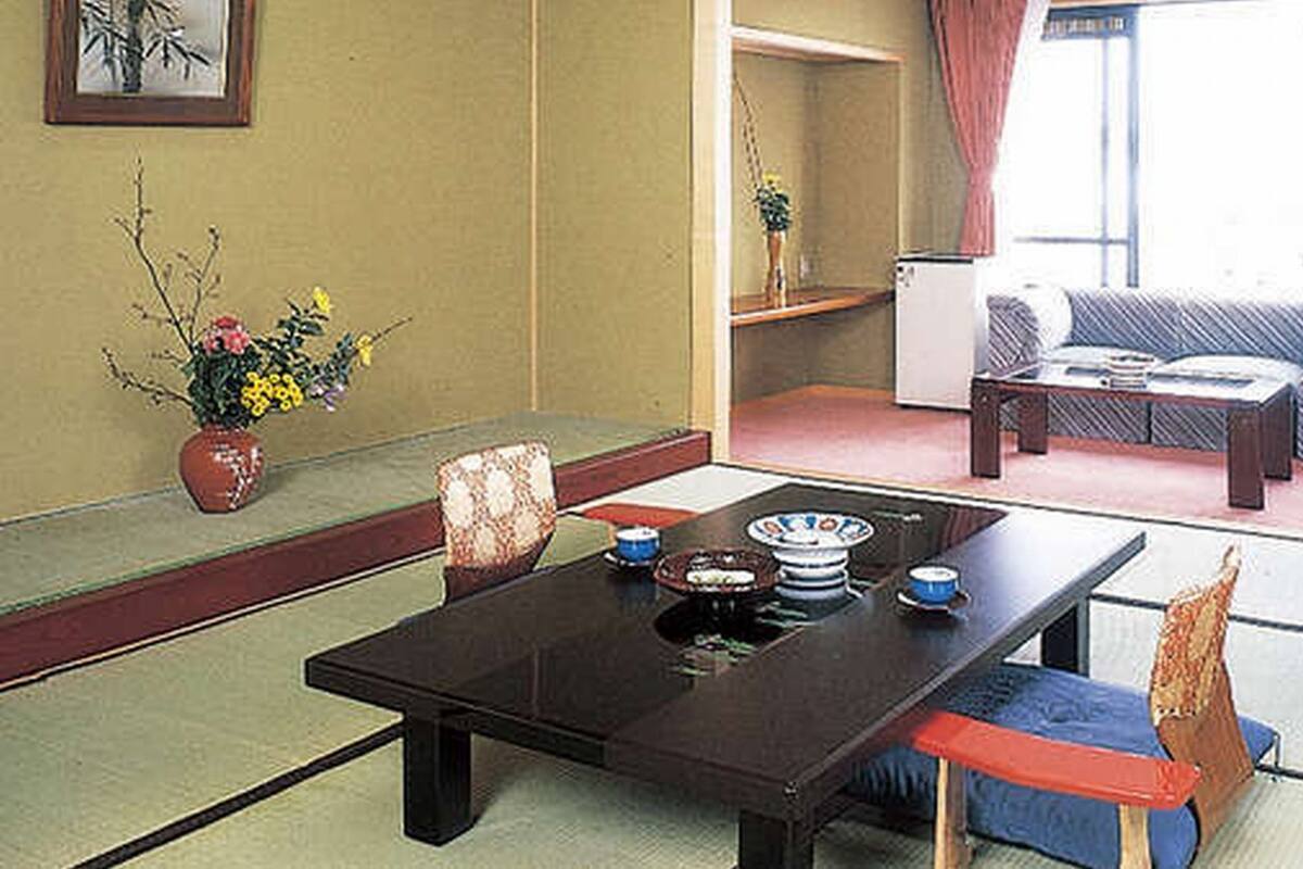 Perinteinen japanilaistyylinen huone, jossa on tatamimatto, matala pöytä teekupit ja -tarvikkeineen, sohva ja pieni kaappi.