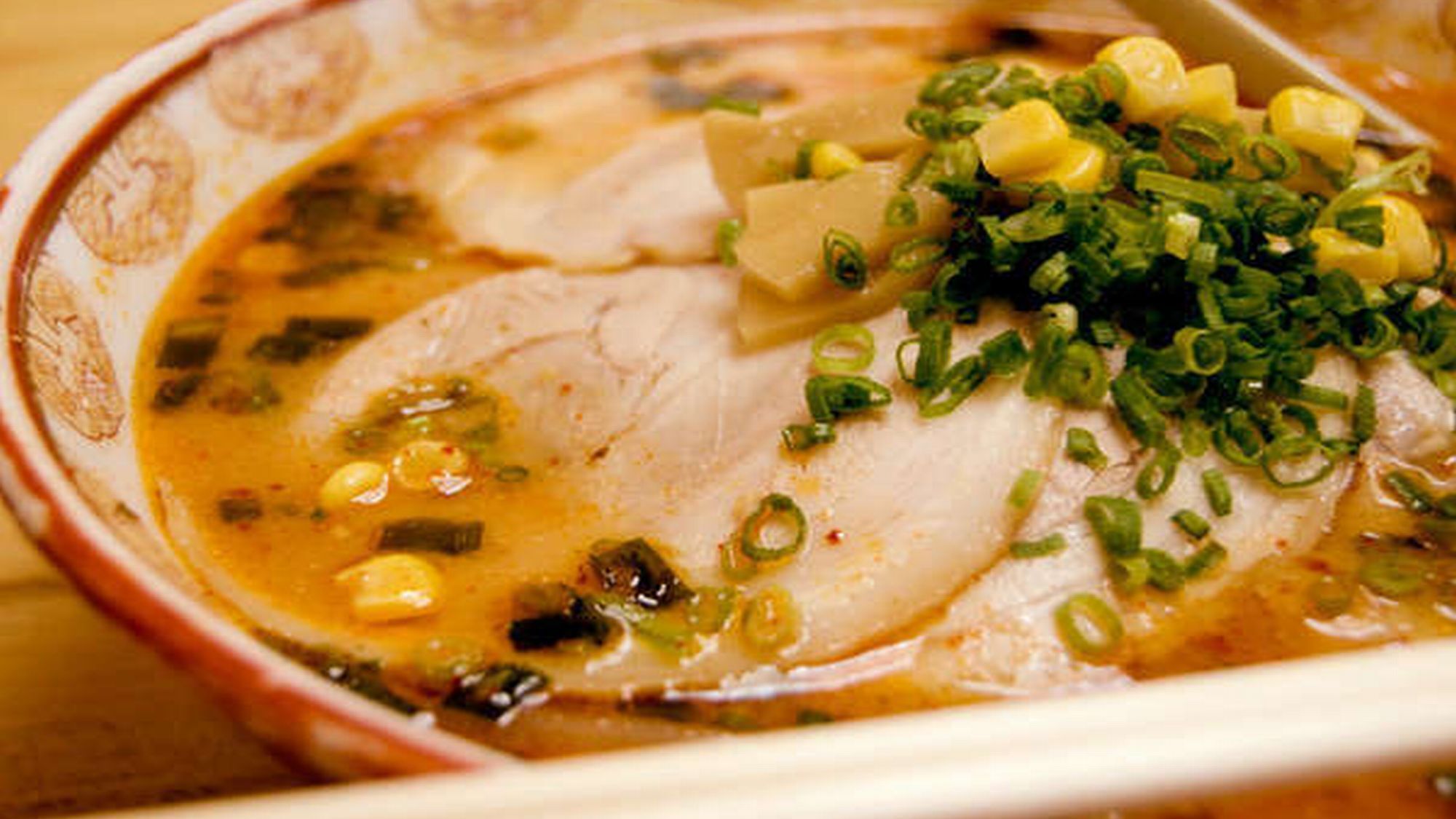 A bowl of soup with a slice of meat, corn, and green onions.