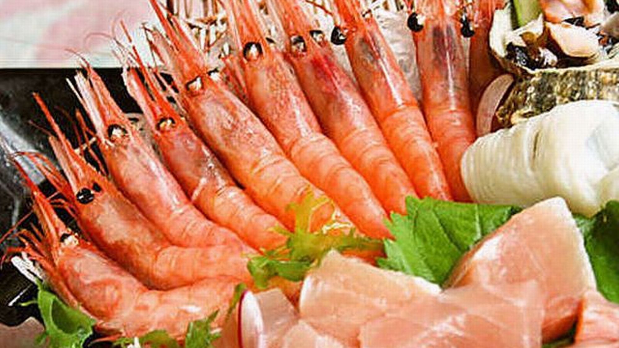 A variety of seafood including prawns, clams, and fish, arranged on a plate with greens and other garnishes.