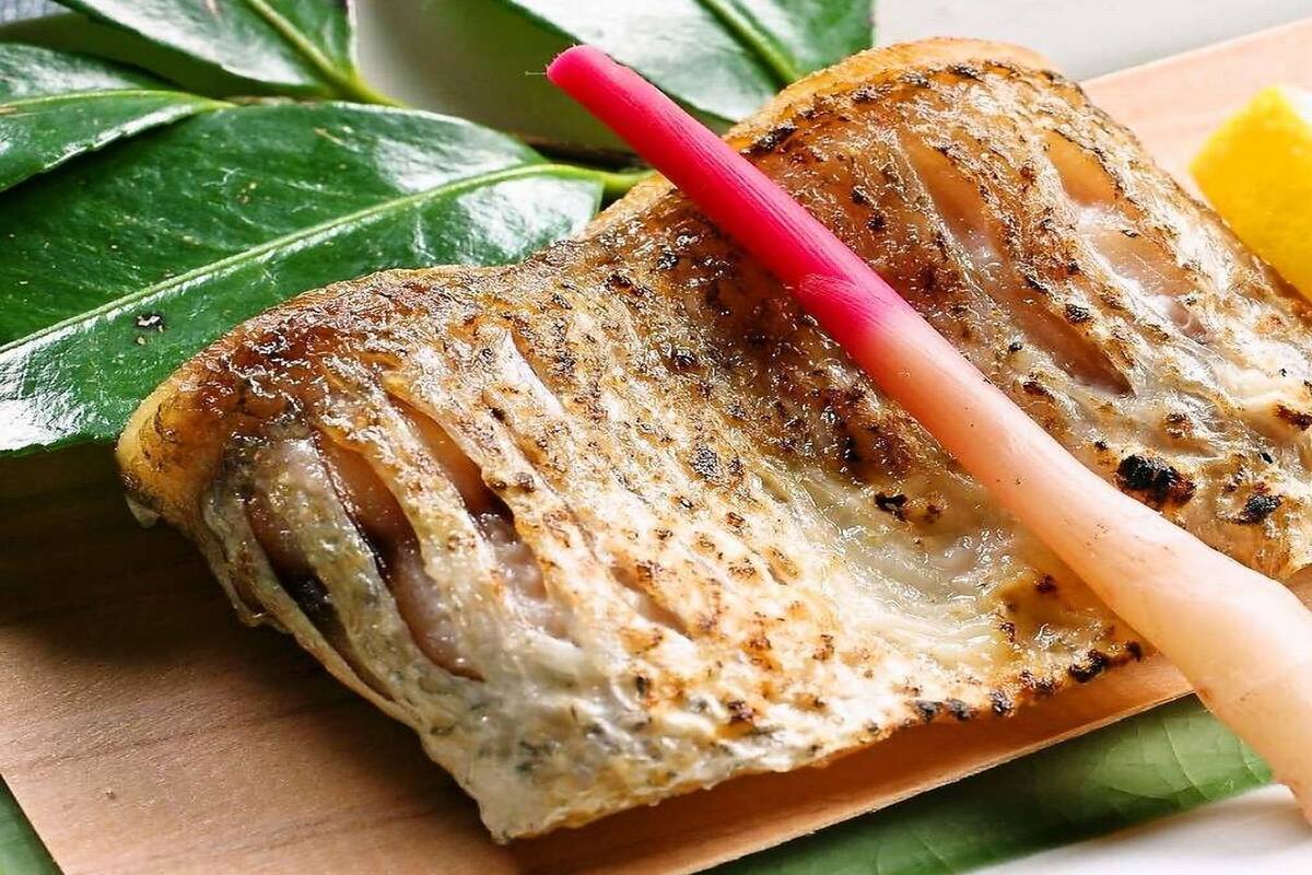 Grillattua kalaa tarjoillaan puulautalla, koristeena sitruunaviipale ja punainen pilli.