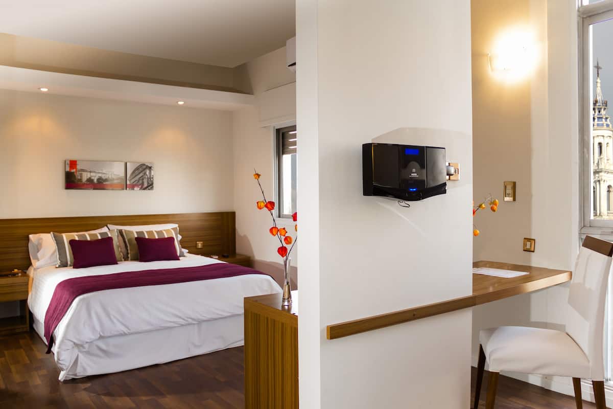 Habitación de hotel con cama, escritorio, silla, televisor y ventana con vista a un edificio.