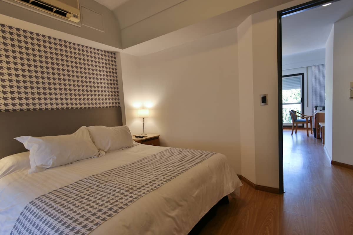 Habitación de hotel con una cama grande, un cabecero estampado, una lámpara de noche y vistas al comedor.