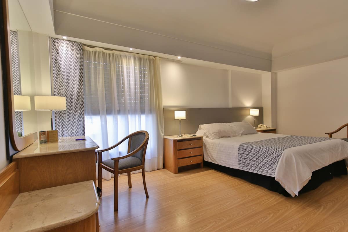 Una habitación de hotel con cama, mesitas de noche, escritorio, silla y espejo.