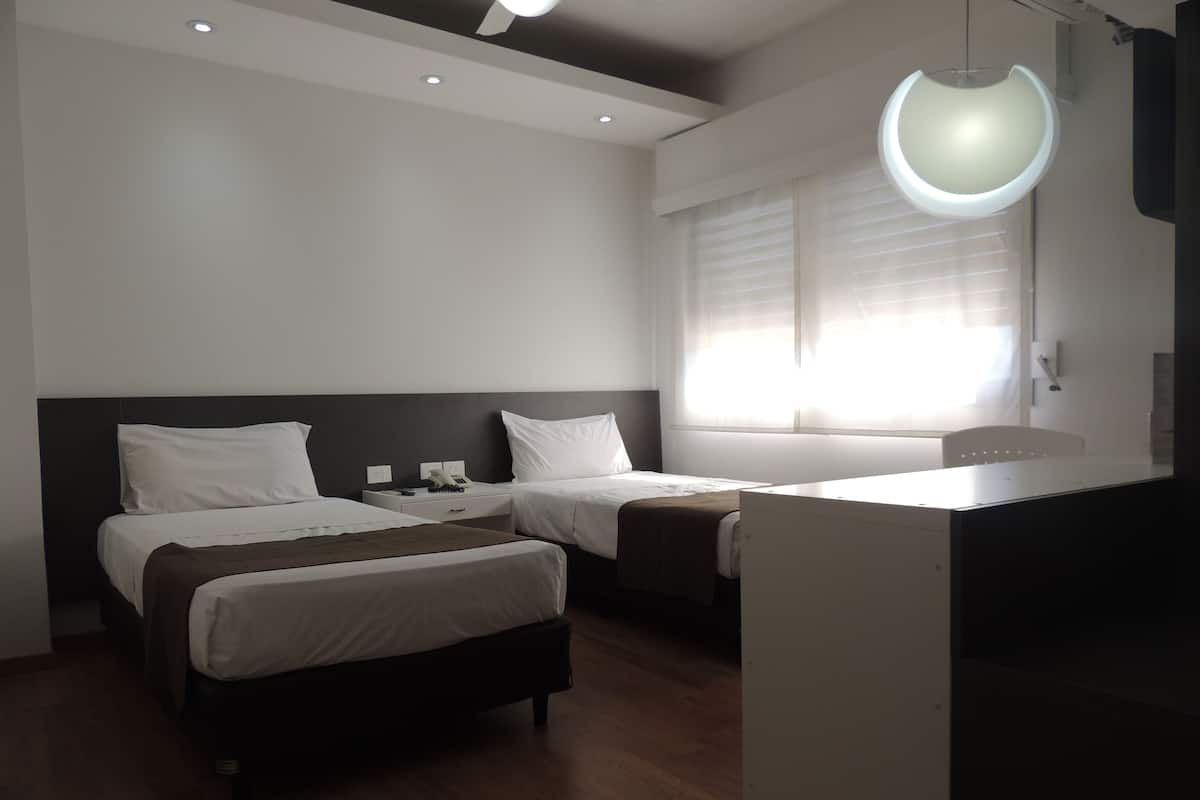 Habitación de hotel con dos camas, un escritorio y un ventanal grande con persianas.