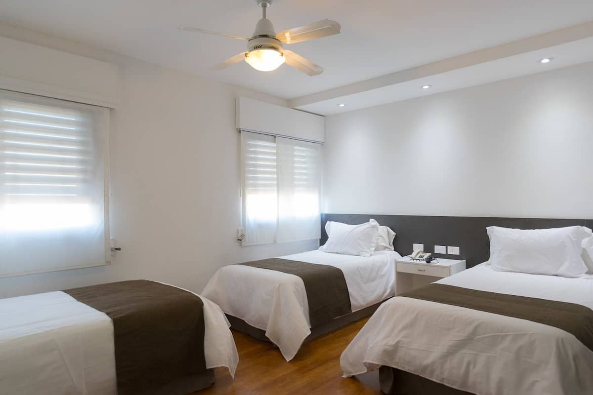 Habitación de hotel con dos camas, un ventilador de techo, una mesita de noche con teléfono y una ventana con persianas.