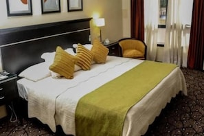 A hotel room with a bed, a chair, a nightstand, and a lamp.