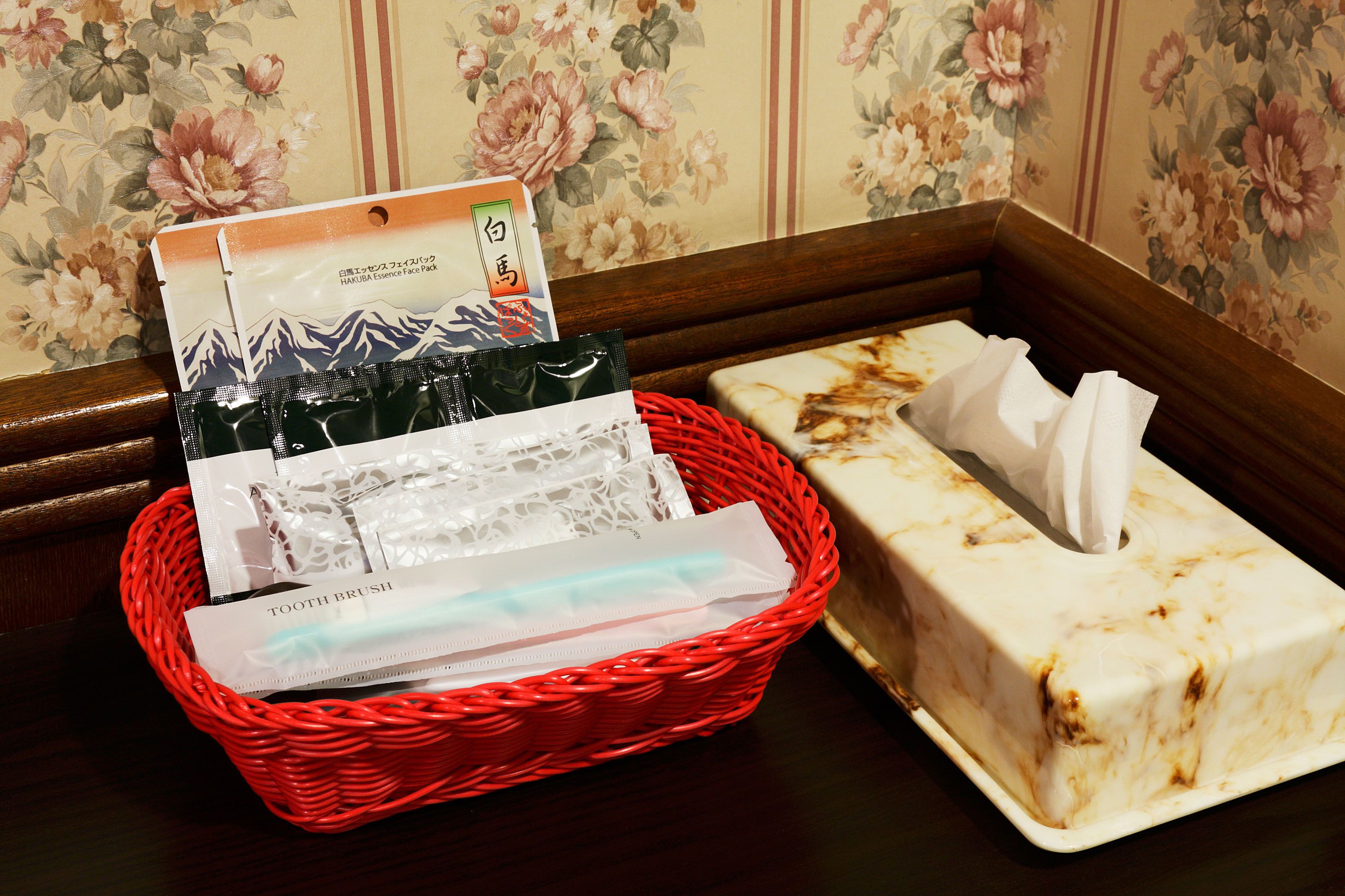 A red wicker basket containing a face mask, a tissue, and a toothbrush.
