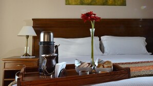 A hotel room with a wooden bedside table, a lamp, a tray with bread, a vase with flowers, and a painting on the wall. - La Campiña Club Hotel & Spa (Santa Rosa de Toay)
