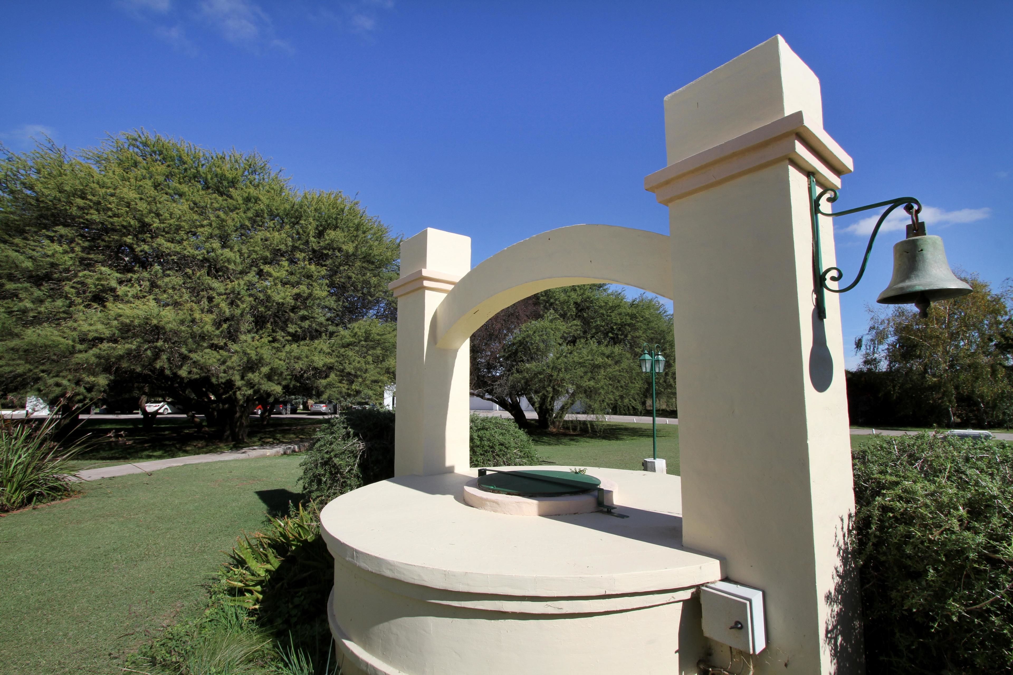 A gazebo with a bell, surrounded by greenery and trees.
