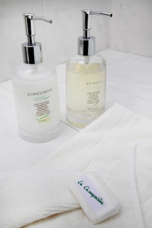 Two bottles of shampoo and conditioner on a white surface with a white towel and a soap bar. - La Campiña Club Hotel & Spa (Santa Rosa de Toay)