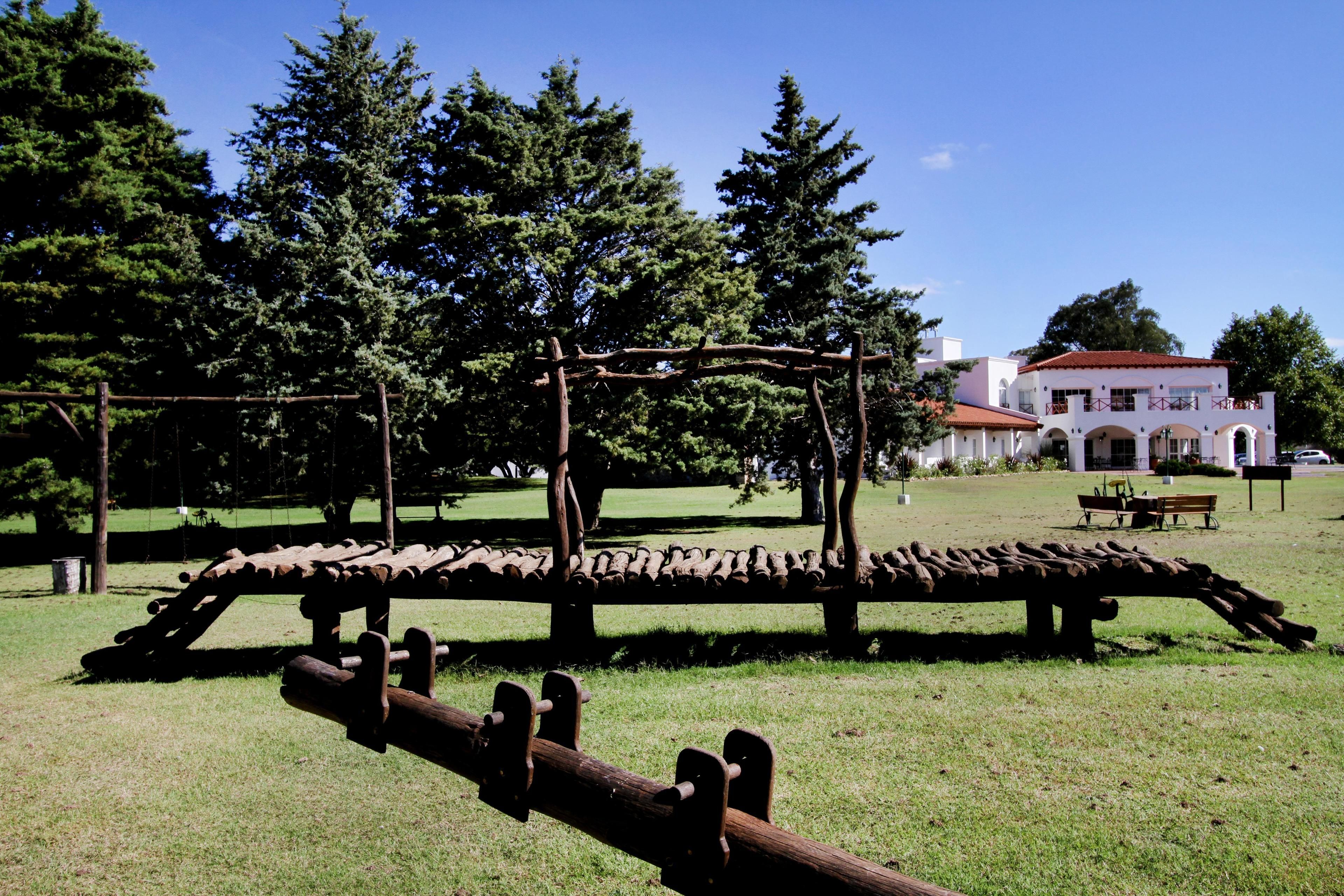 A rustic wooden bench in a park with a white building in the background.