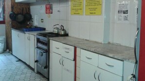 A kitchen with white cabinets, a stove, and a sink. There are signs on the wall and a red trash bin. - Hostel Campo Base (Mendoza City)