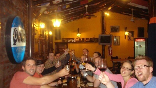 A group of people toasting at a bar with a sign reading "Traveller's Bar". - Hostel Campo Base (Mendoza City)