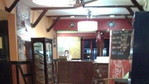 A restaurant interior with a wooden floor, a counter with a person behind it, and a menu board on the wall. - Hostel Campo Base (Mendoza City)