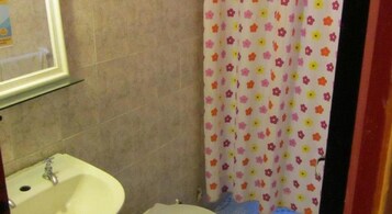Un baño con lavamanos blanco, espejo y cortina de ducha con estampado floral.