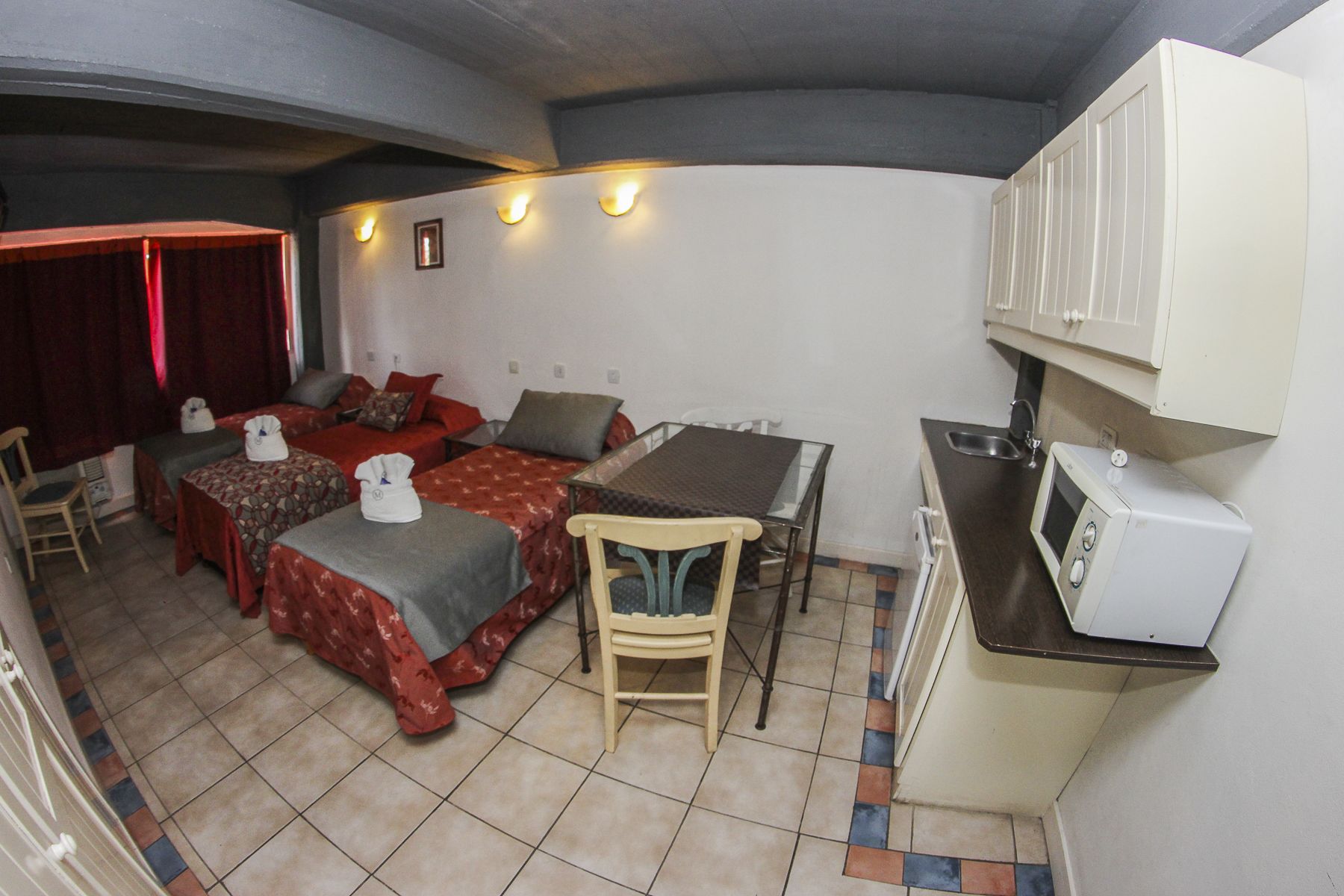 A compact room with two beds, a small table, a chair, a microwave, and a sink.