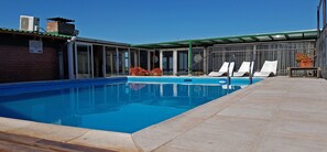 A swimming pool with lounge chairs and a covered area.