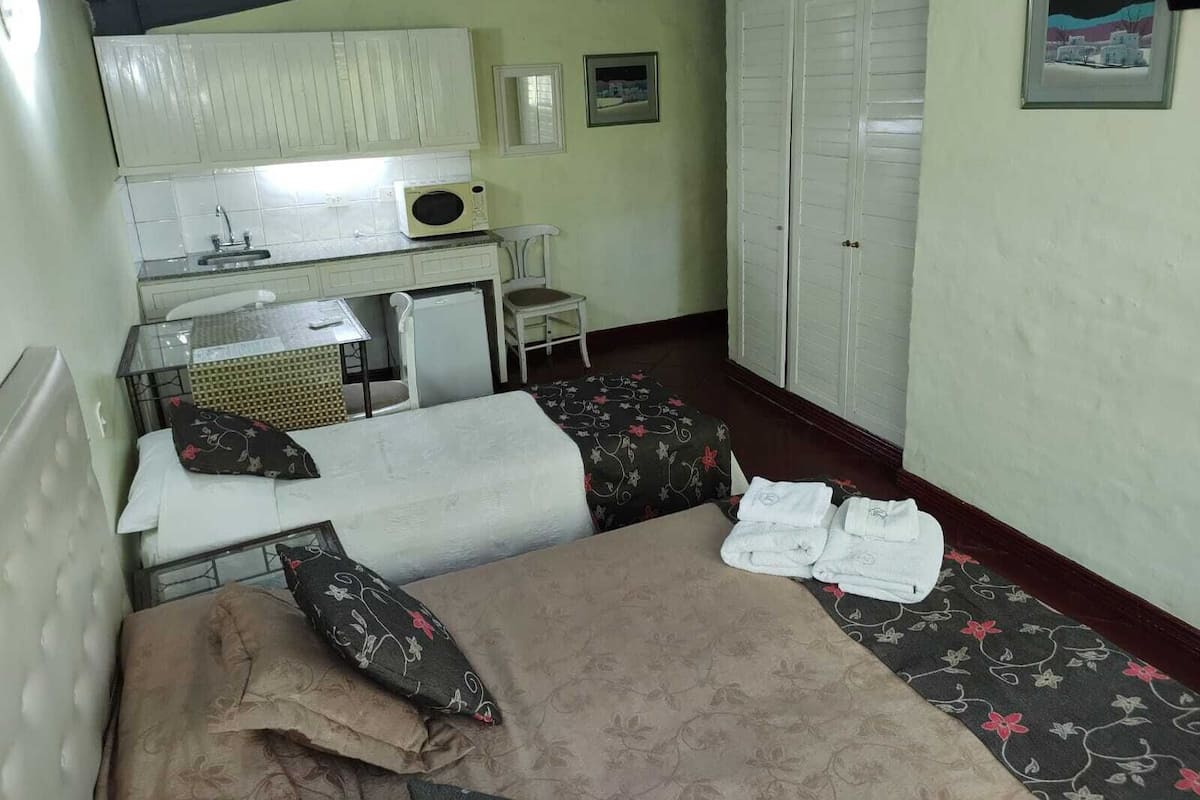 Una habitación compacta con cama, un escritorio pequeño con silla, microondas y armario.