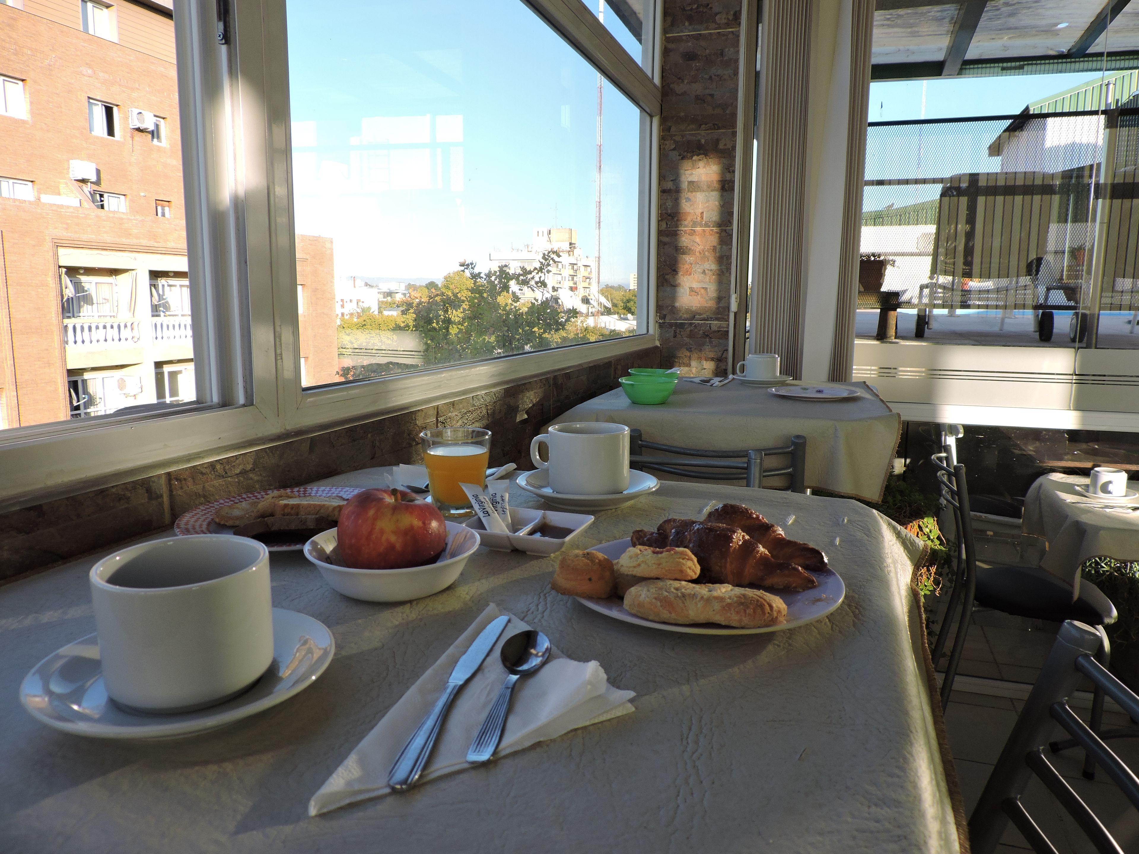 A breakfast table with a cup, a bowl of fruit, and pastries, set against a city view.