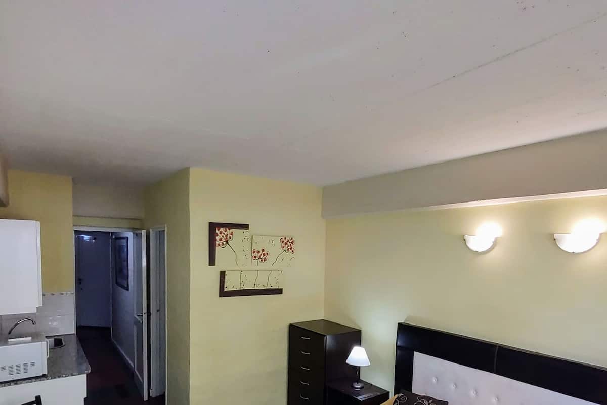 Una habitación de hotel con cama, mesita de noche, lámpara y un pequeño escritorio con silla.