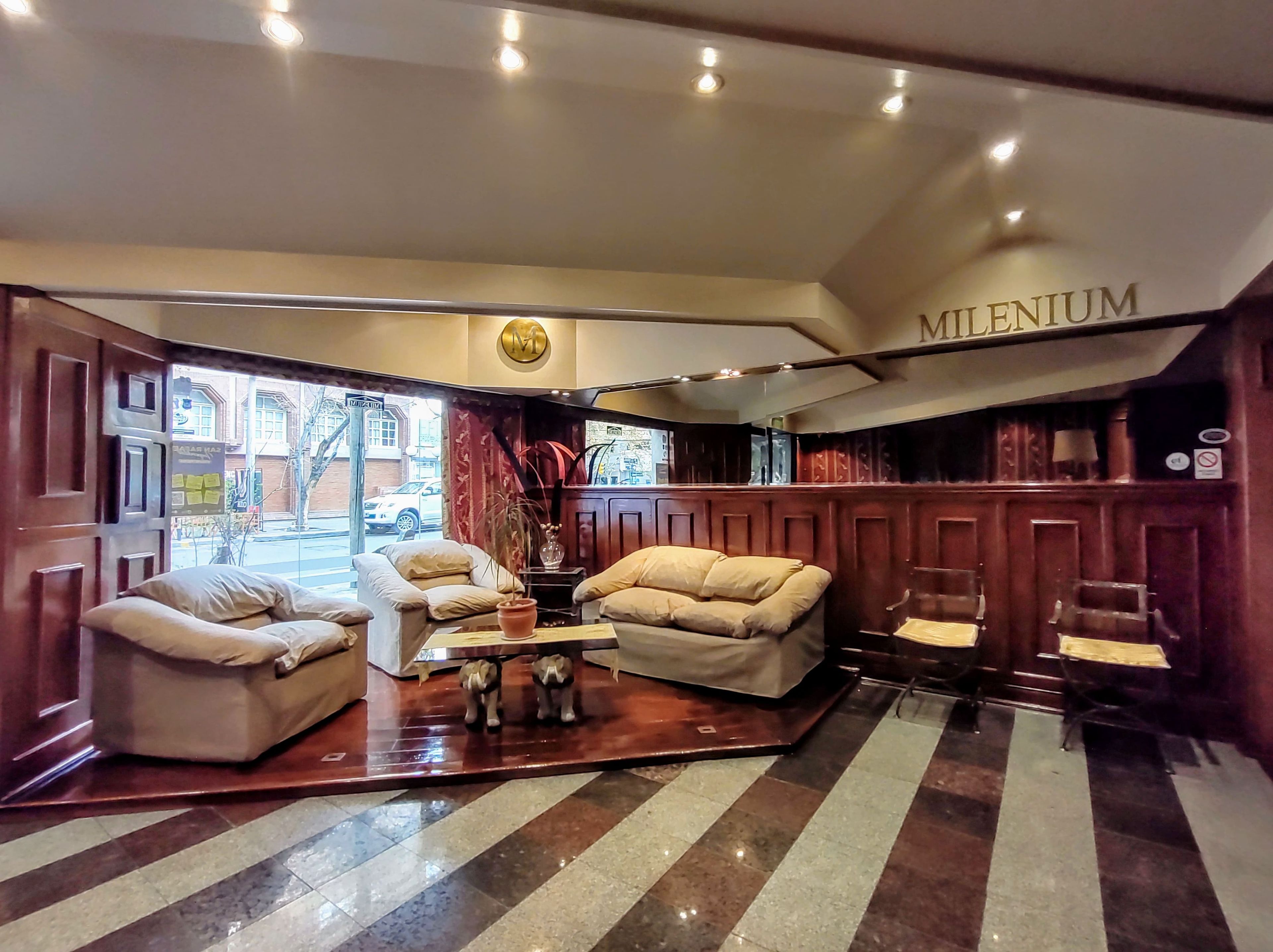 A hotel lobby with a seating area, a reception desk, and a view of the street outside.