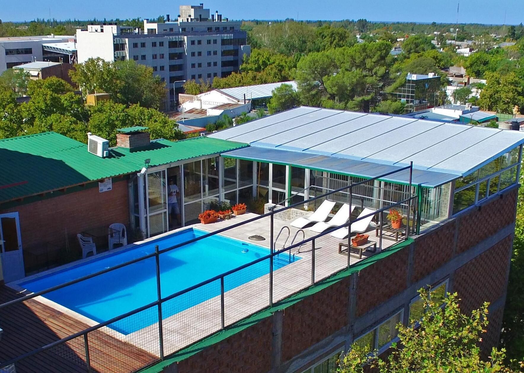 Piscina en la azotea con cerramiento de vidrio, rodeada de sillas de descanso y plantas en macetas.