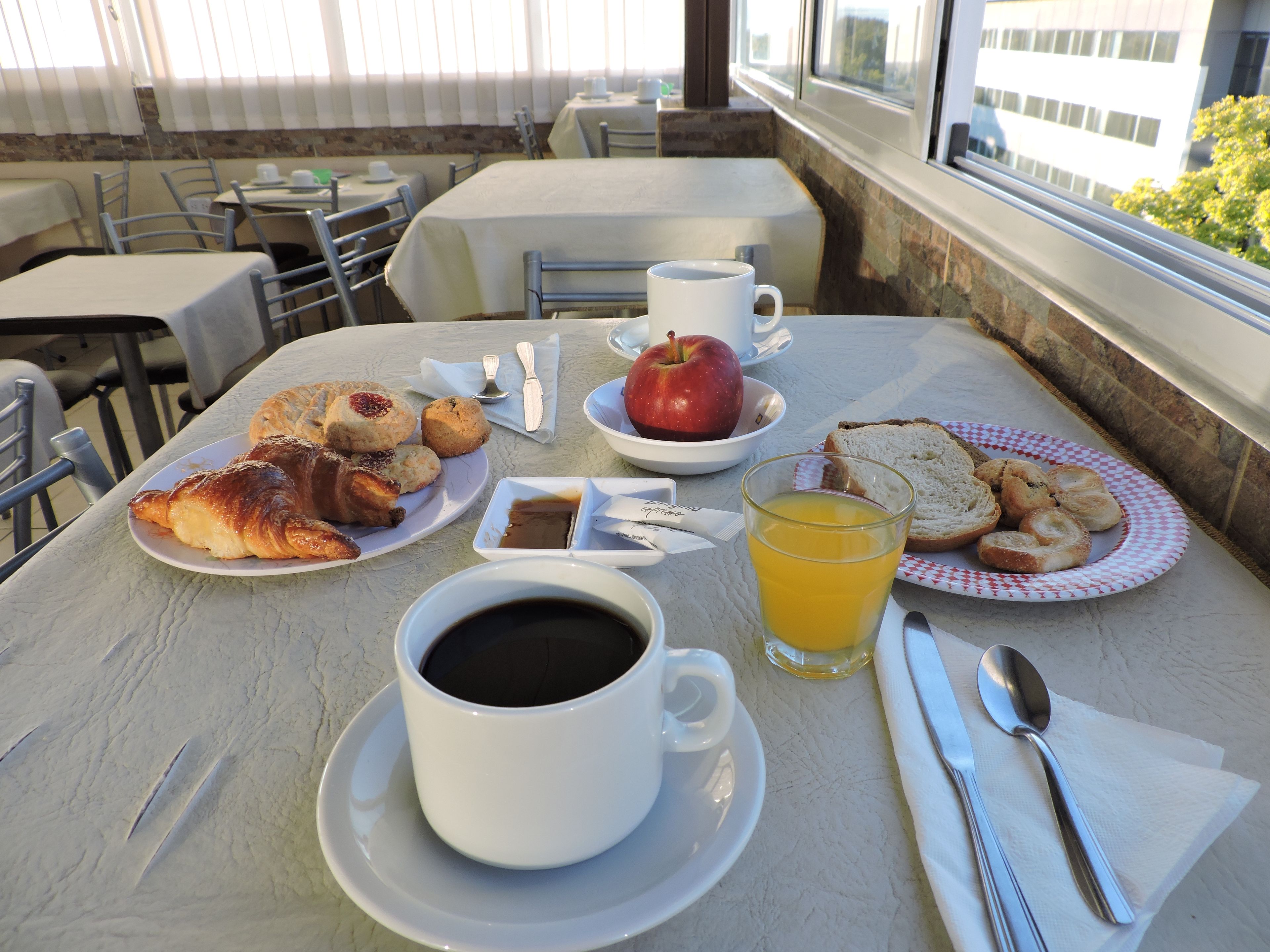 A breakfast table with croissants, a glass of orange juice, a cup of coffee, and a plate of toast.