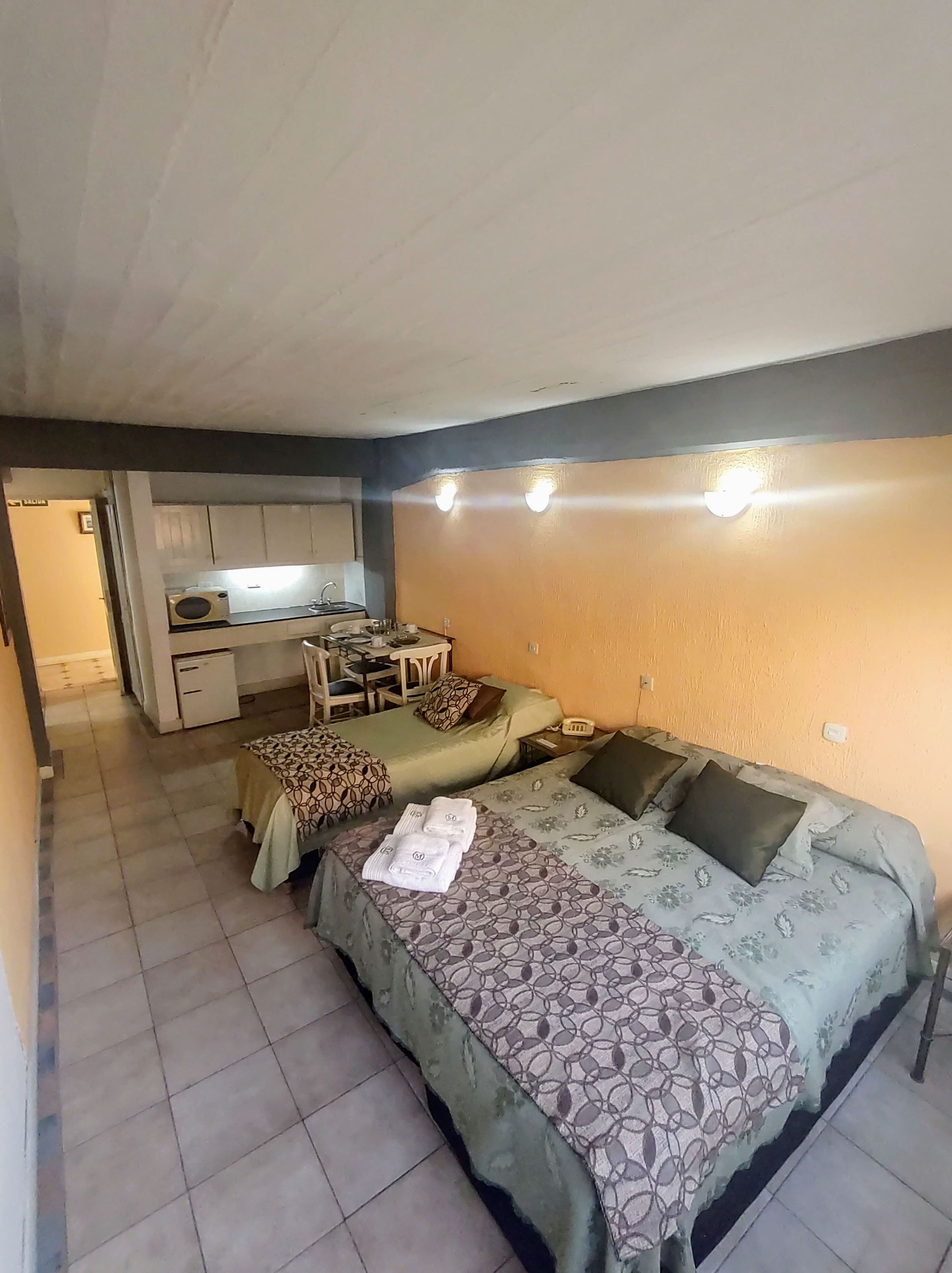 A compact room with two beds, a small kitchenette, and a dining area.