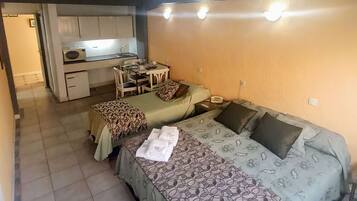 A compact room with two beds, a small kitchenette, and a dining area.