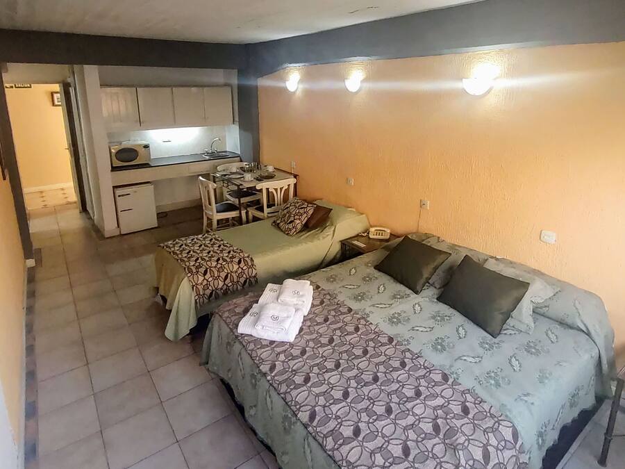 A compact room with two beds, a small kitchenette, and a dining area.