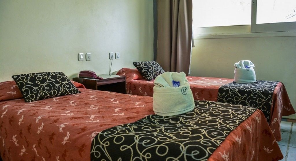 Habitación de hotel con dos camas, cada una con ropa de cama estampada, una mesita de noche con teléfono y una ventana con cortinas.