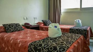 Habitación de hotel con dos camas, cada una con ropa de cama estampada, una mesita de noche con teléfono y una ventana con cortinas.