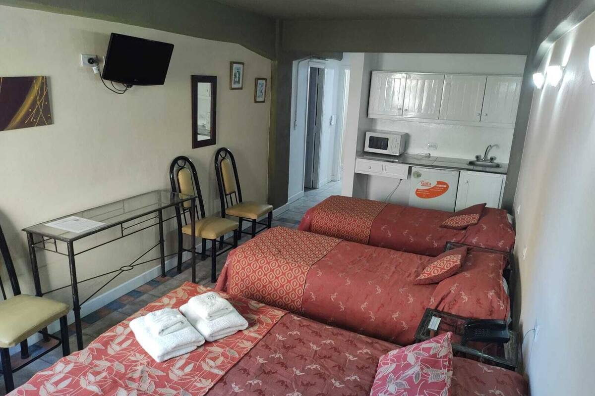 Una habitación con dos camas, un escritorio con sillas, televisión y kitchenette.