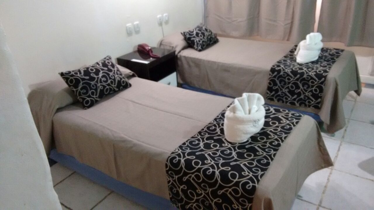 A hotel room with two beds, each with a patterned bedspread and a towel on the bed. There is a nightstand with a phone and a red object on it.