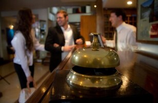 A hotel reception area with a bell on a stand, a counter, and a few people in the background.