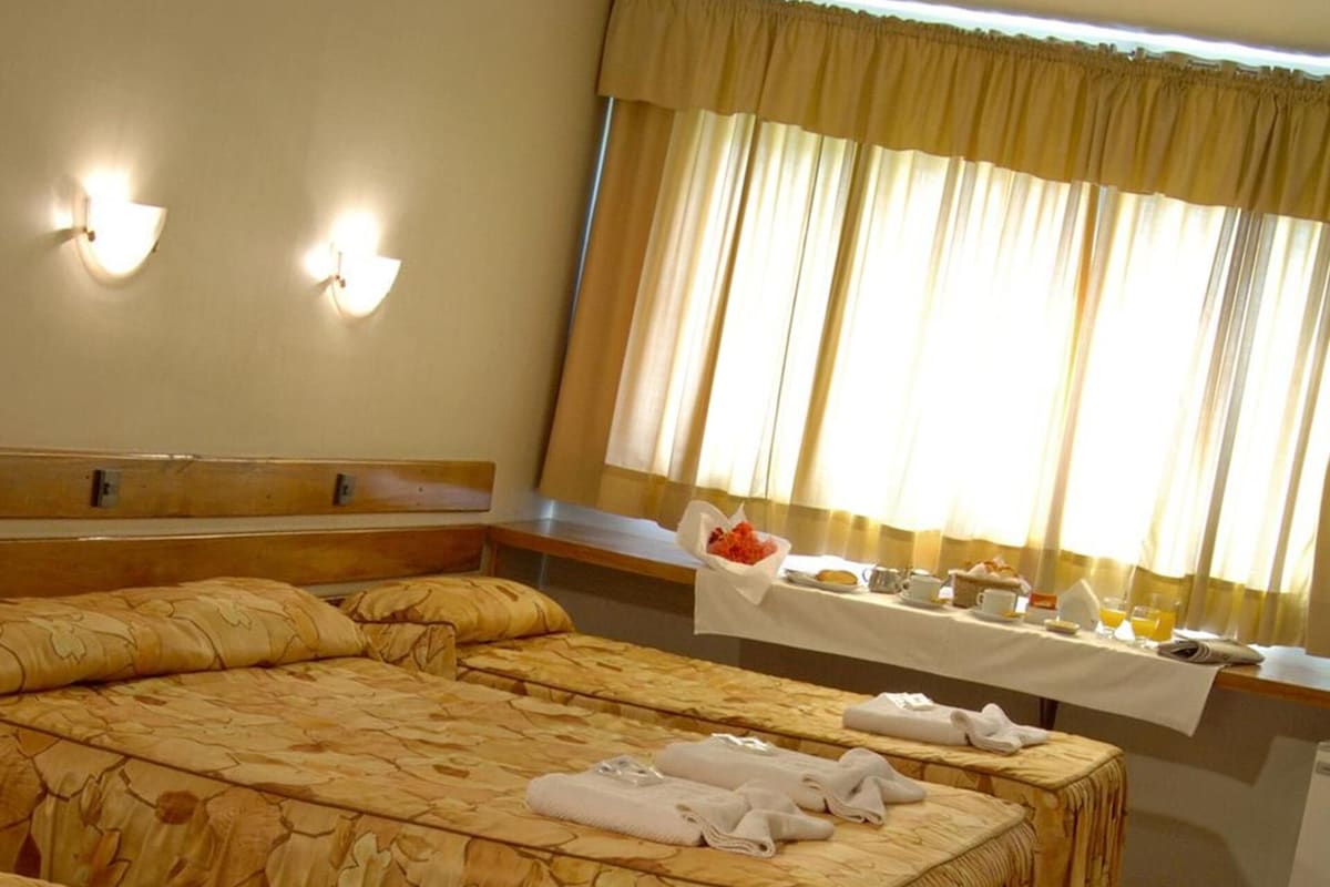 A hotel room with four beds, each with a floral bedspread and white towels. There is a breakfast table with various breakfast items and a chair.