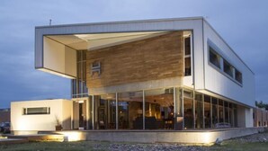 A modern two-story building with a large glass facade, a prominent 'H' logo, and a flat roof. - Herradura Hotel Suites (Neuquen)