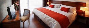 Una habitación de hotel con una cama grande, dos lámparas de noche, una silla y un escritorio con lámpara.