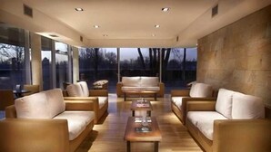 A modern interior with sofas and a coffee table, large windows, and a stone wall. - Herradura Hotel Suites (Neuquen)