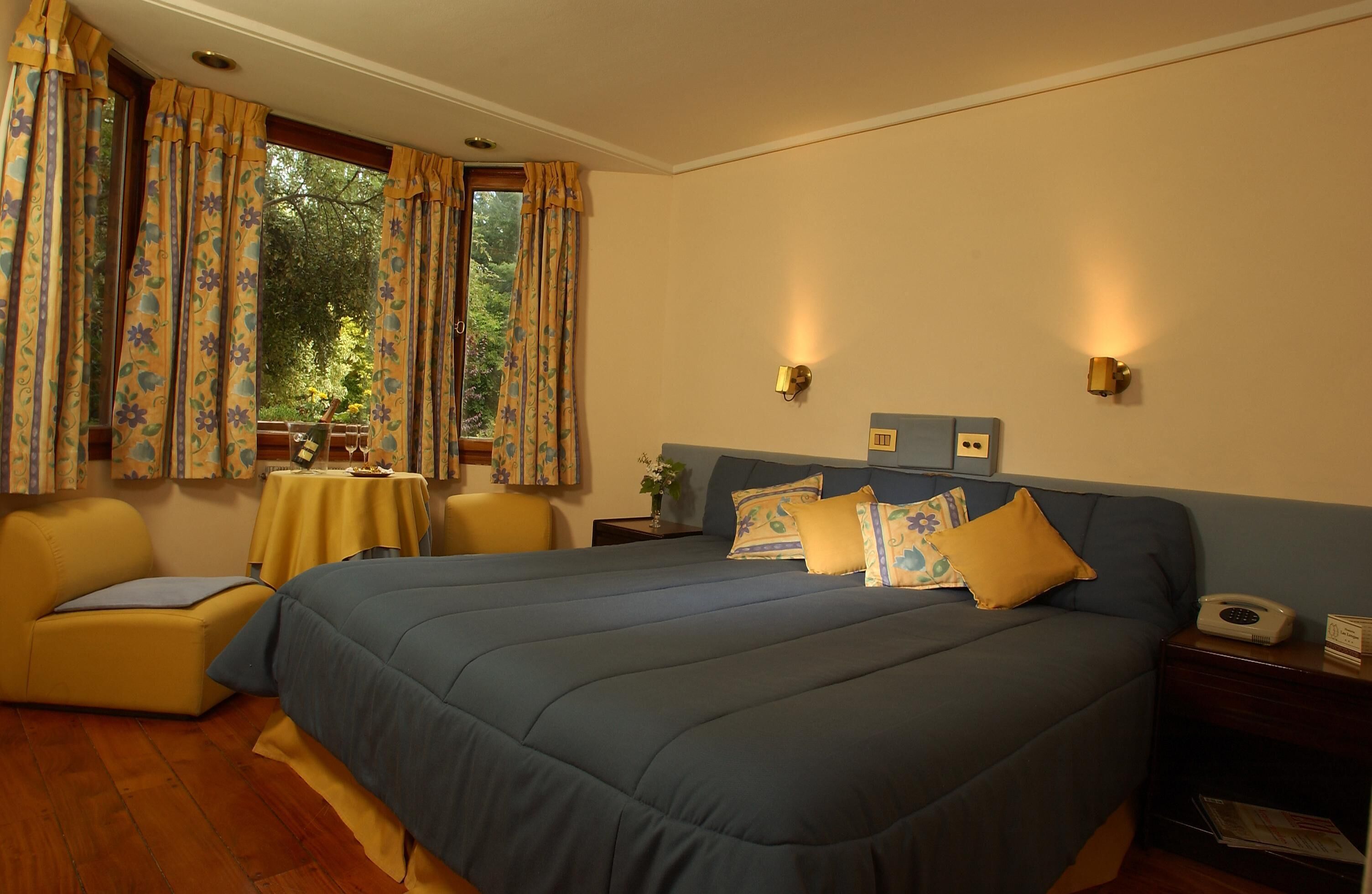 A bedroom with a large bed, a bedside table with a lamp, a chair, and a window with curtains.