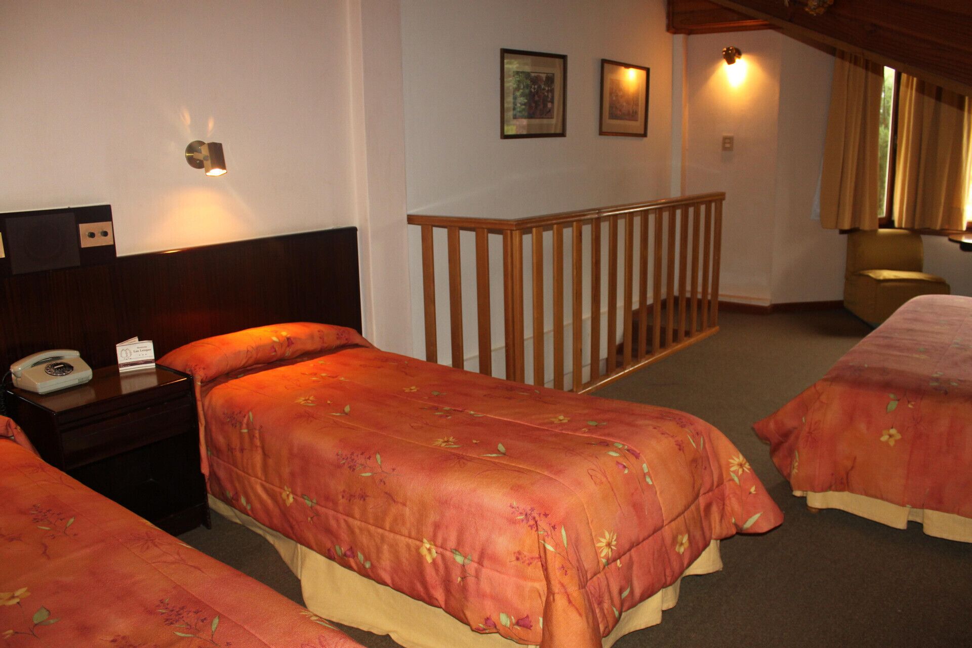 A hotel room with two beds, a wooden headboard, a nightstand with a telephone, and a staircase leading to another room.