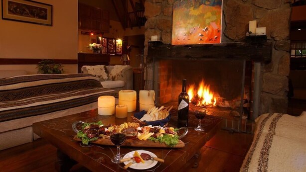 Une pièce chaleureuse avec une cheminée en pierre, une table à manger dressée avec de la nourriture et du vin, et un tableau accroché au-dessus de la cheminée.