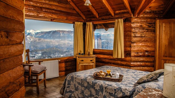 Une chambre de style rustique, avec un lit, une chaise, une table de chevet et une fenêtre avec des rideaux.
