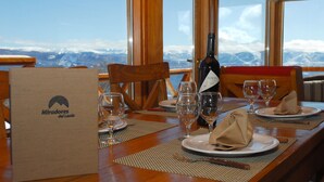 Une table à manger dressée avec des assiettes, des verres et une bouteille, avec une vue sur les montagnes en arrière-plan.