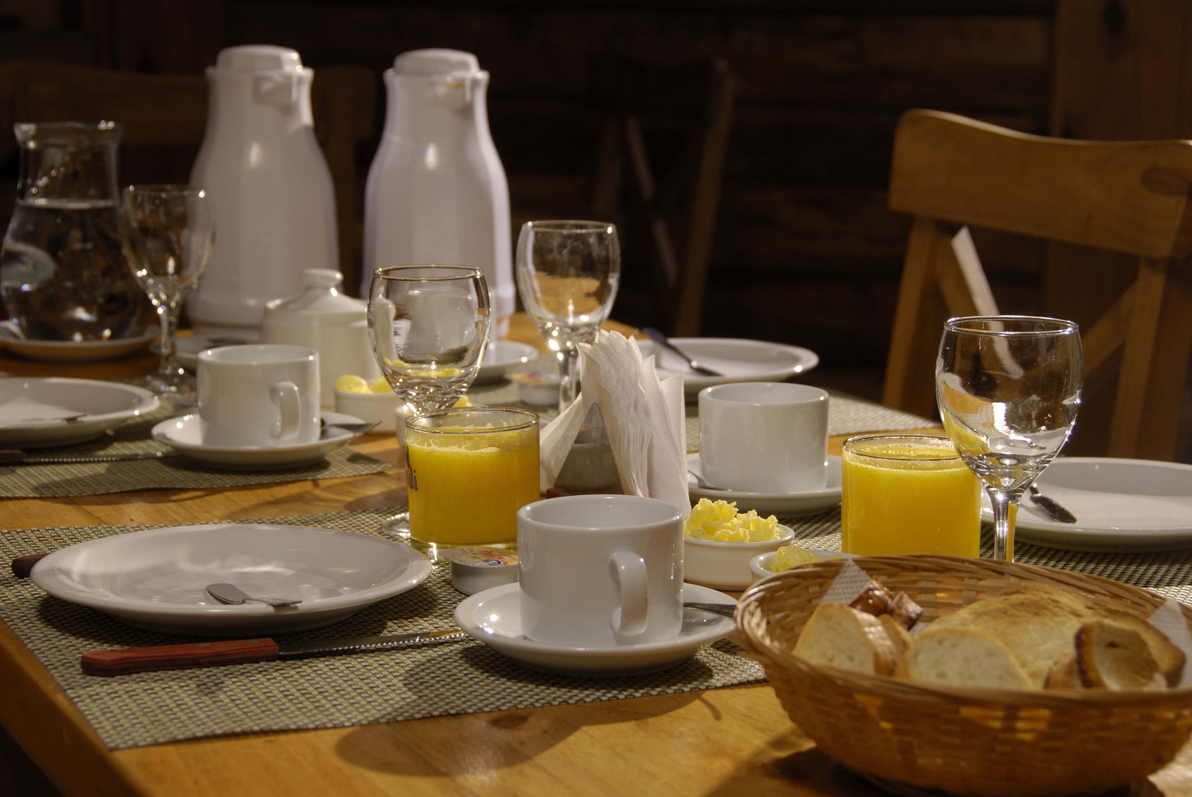 Una mesa para el desayuno servida con platos, tazas, vasos y una cesta de pan.