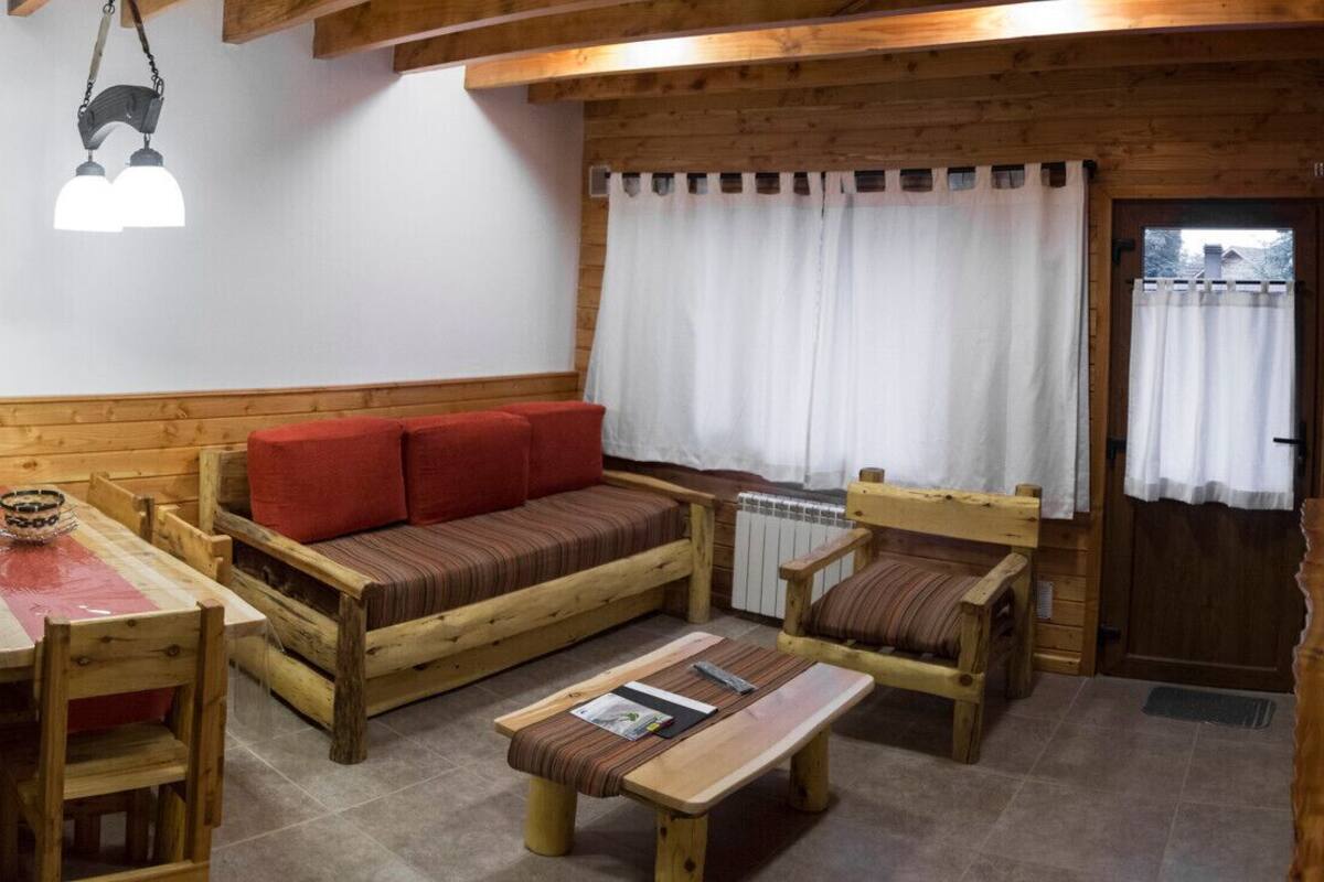 Cocina pequeña con microondas, refrigerador y lavabo. Hay una mesa de comedor de madera con sillas, un sofá rojo y un banco de madera.